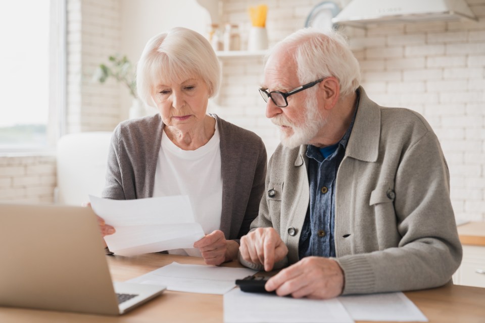 Senior couple looking at papers and using a calculator, with a laptop nearby.