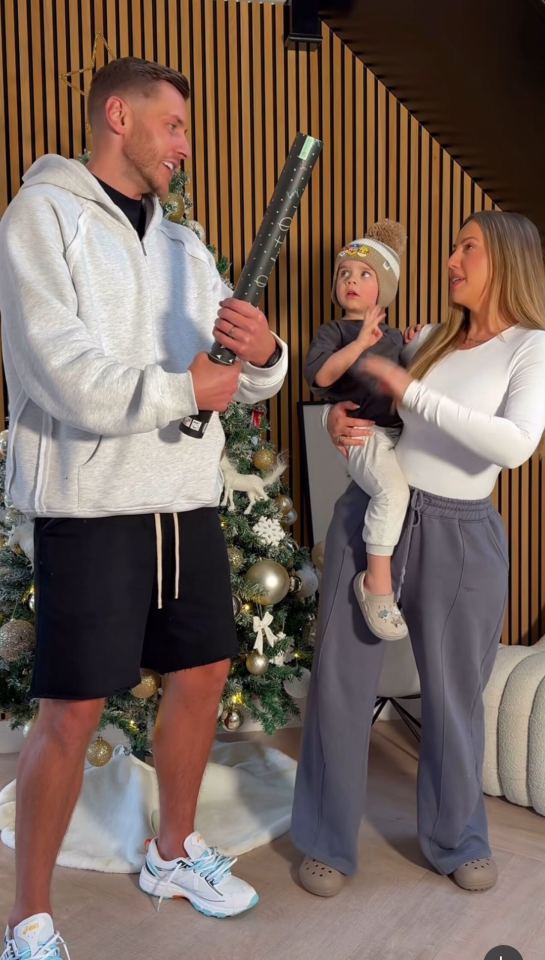 A family of three standing in front of a Christmas tree, with a man holding a confetti popper.