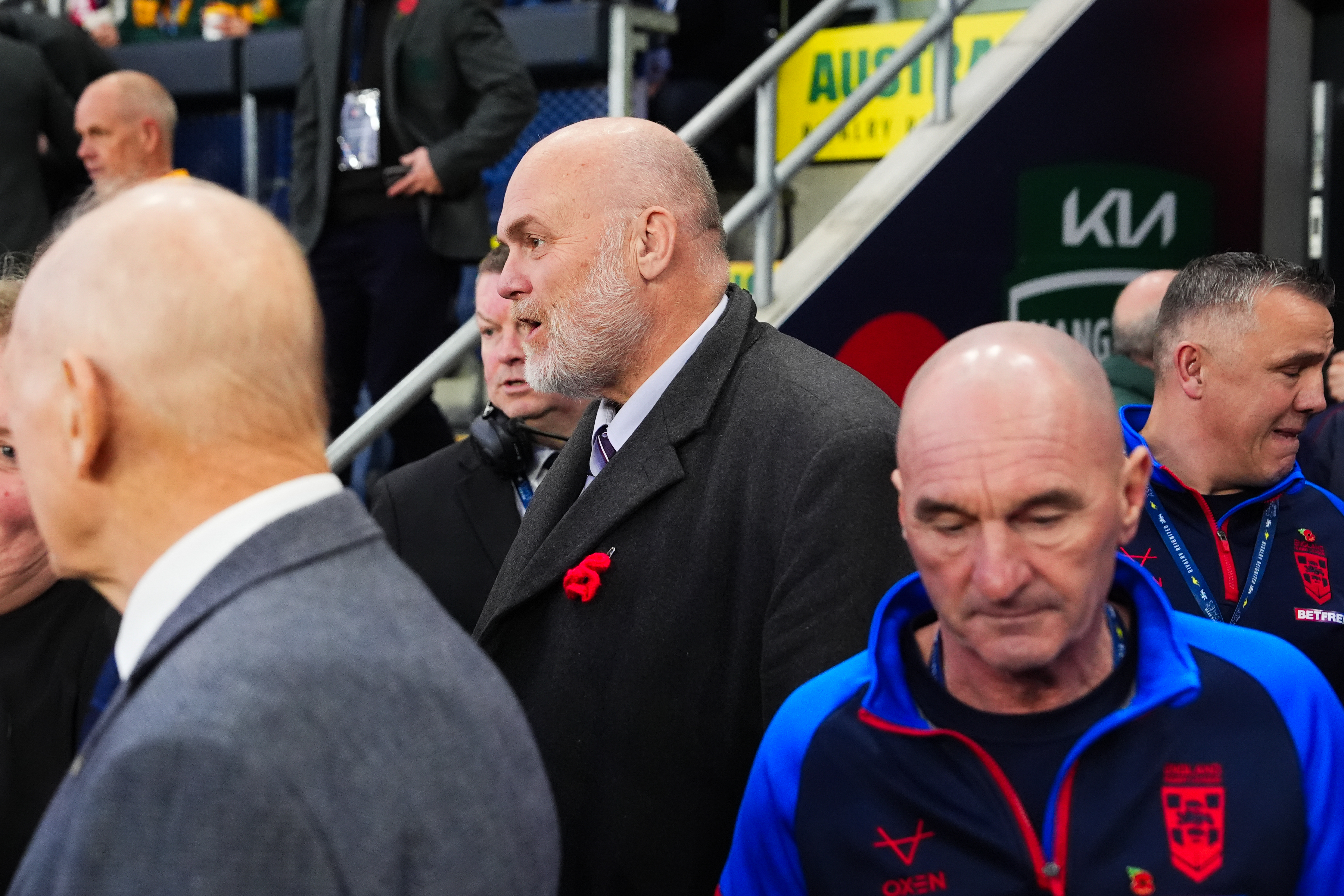 Man with a beard and wearing a poppy pin on his coat, among other spectators at the ABK Beer Rugby League Ashes.