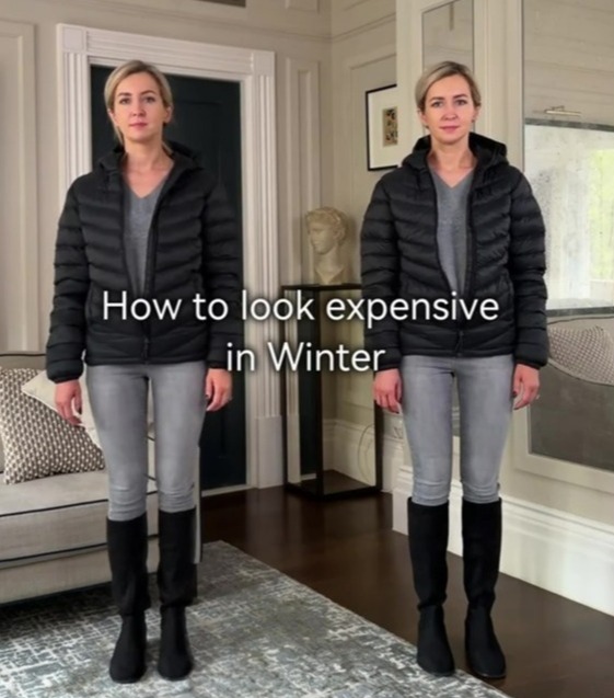 A woman in a black puffer jacket, grey top, grey jeans, and black boots.