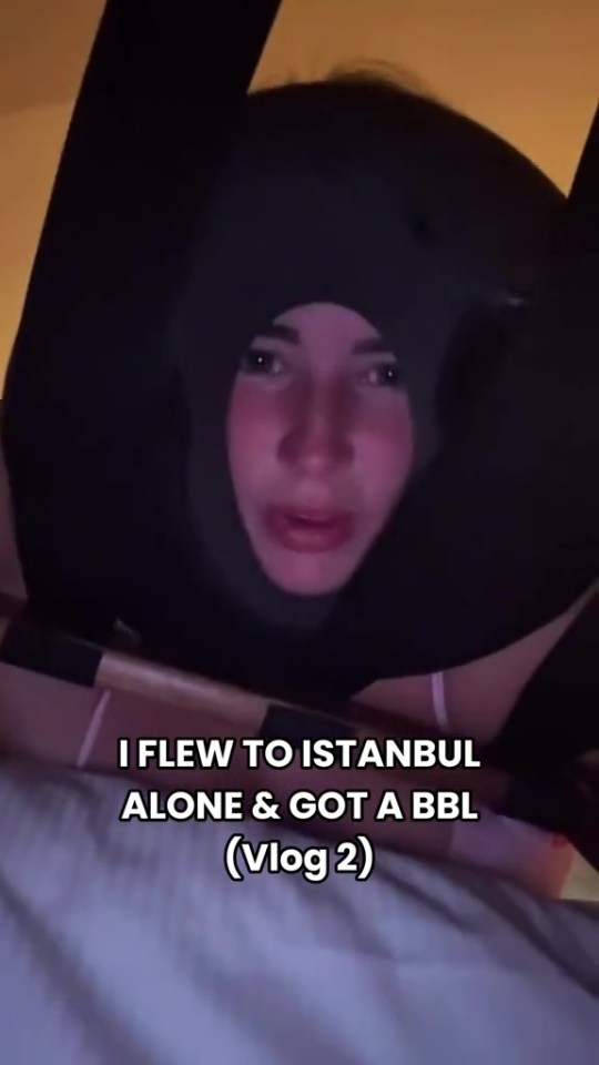 A woman with a dark neck pillow in a dim room with text that reads "I FLEW TO ISTANBUL ALONE & GOT A BBL (Vlog 2)."