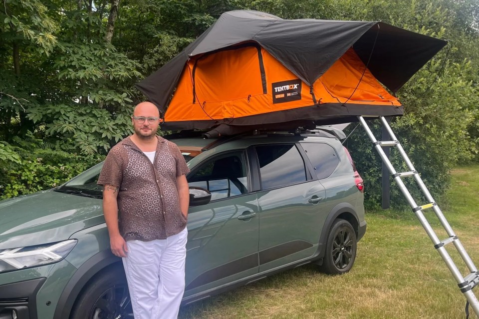 A man standing next to a green car with an orange and black TentBox Lite 2.0 rooftop tent.