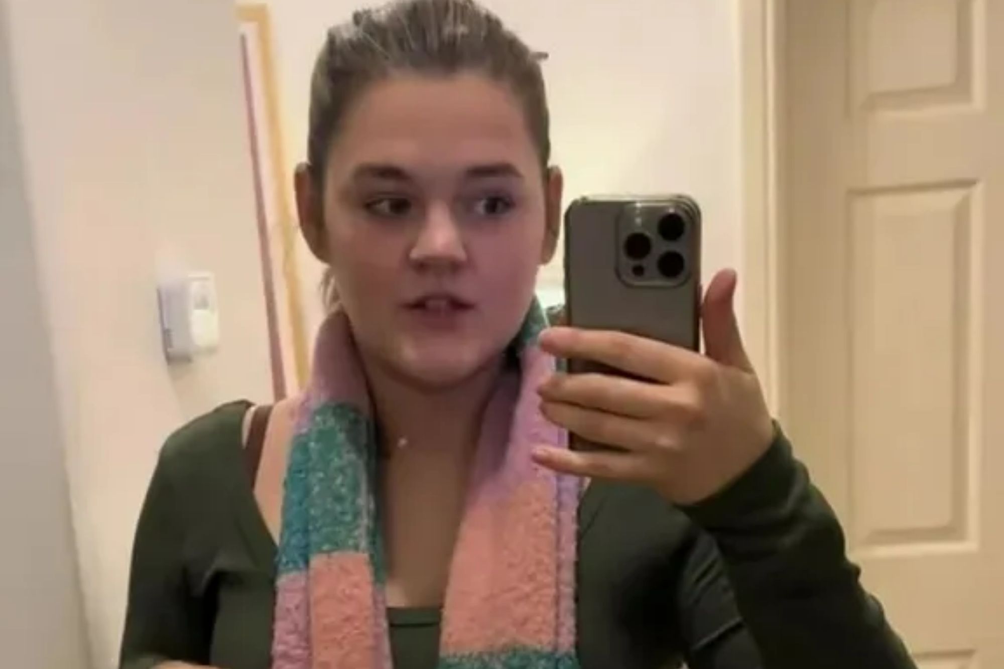 An image collage containing 1 images, Image 1 shows A young woman wearing a long-sleeved shirt, jeans, and a pink and green striped scarf, records herself in a mirror