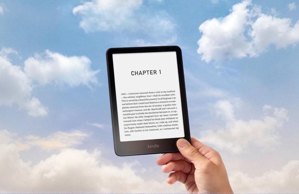 Hand holding a Kindle Paperwhite displaying "Chapter 1" against a cloudy sky.