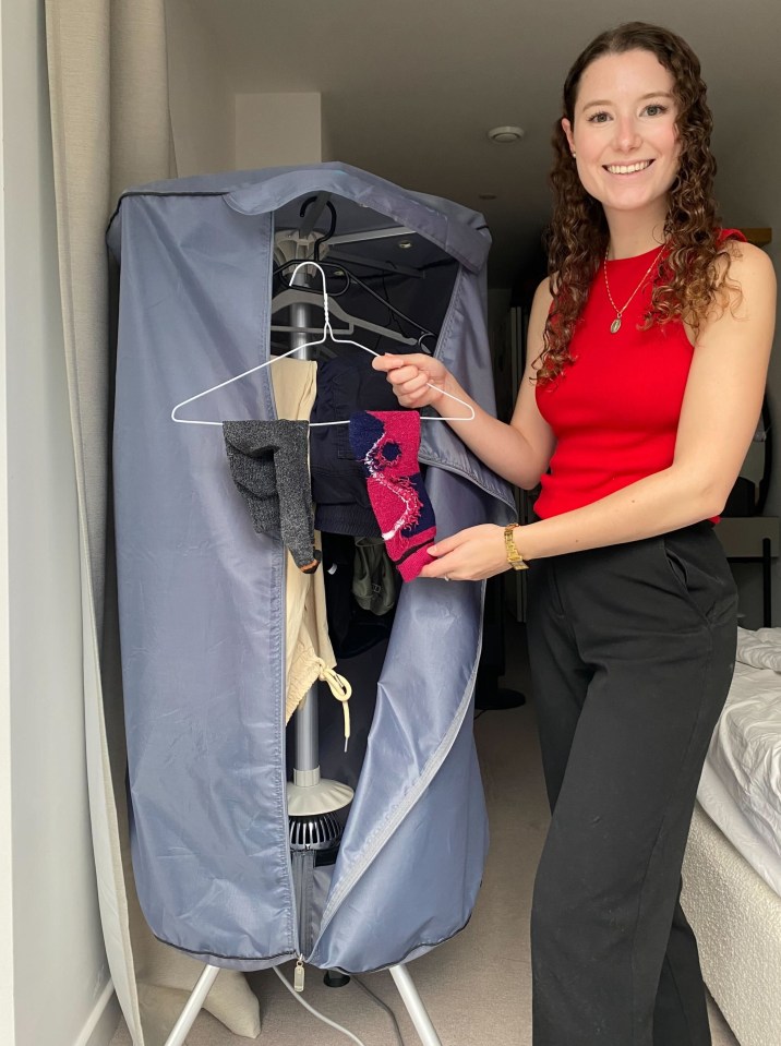 A young woman smiles while holding clothing on a hanger next to a drying cabinet.