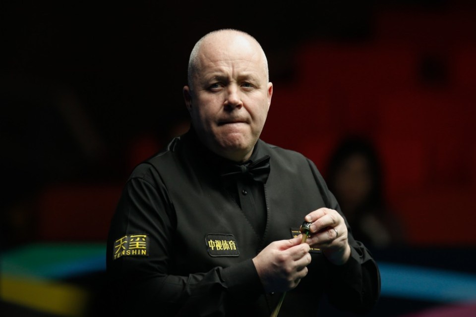 A man in a black vest and bow tie, with a serious expression, is chalking a snooker cue.