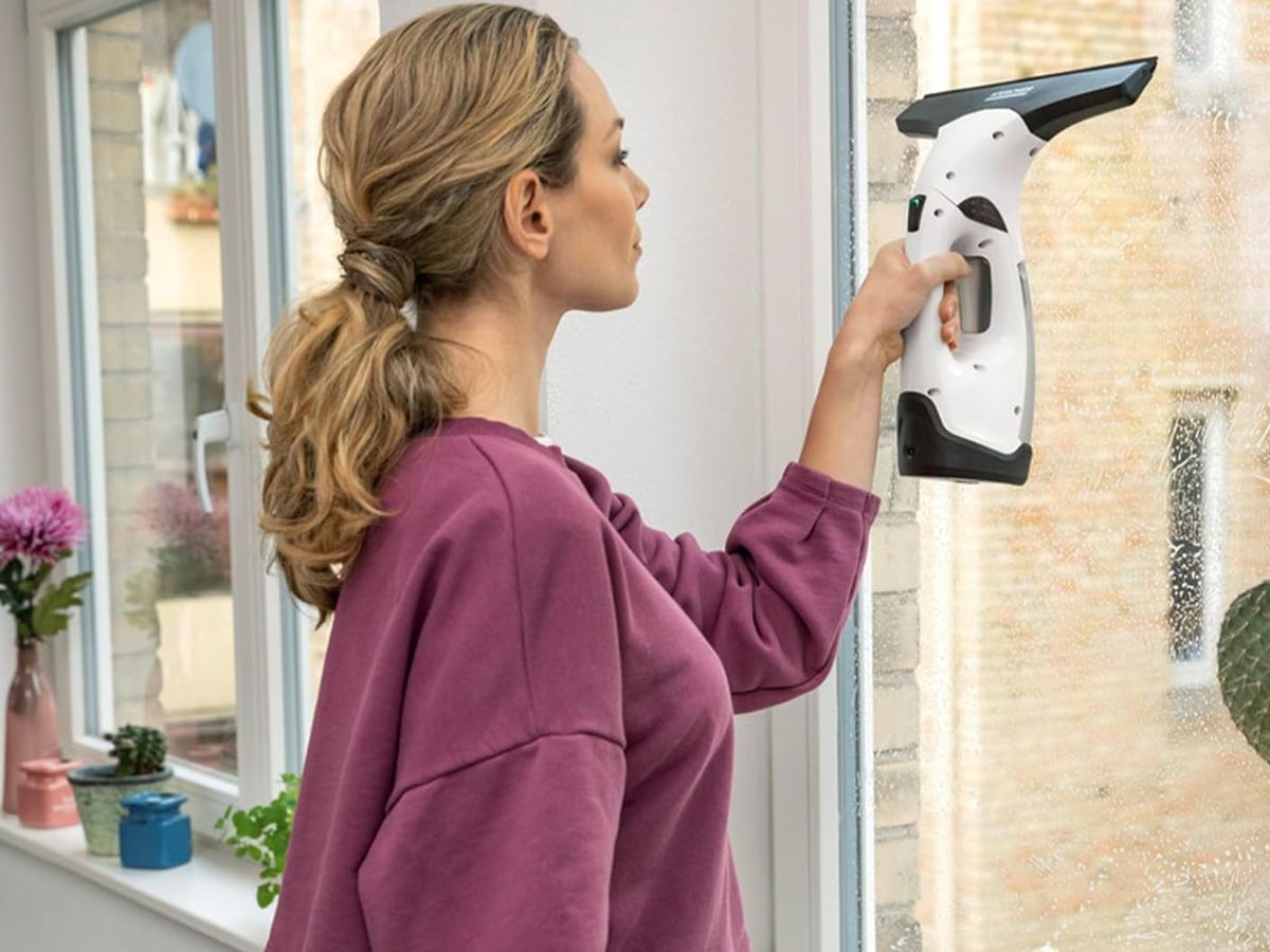 A woman using a handheld window cleaner to clean a window.