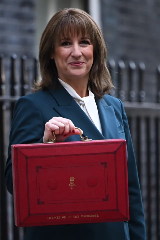 Woman in a blue suit holding the Chancellor of the Exchequer's red budget box.