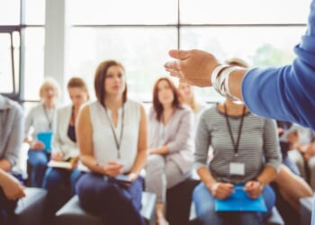 The hand of a trainer addressing a group of females sitting in a conference hall.