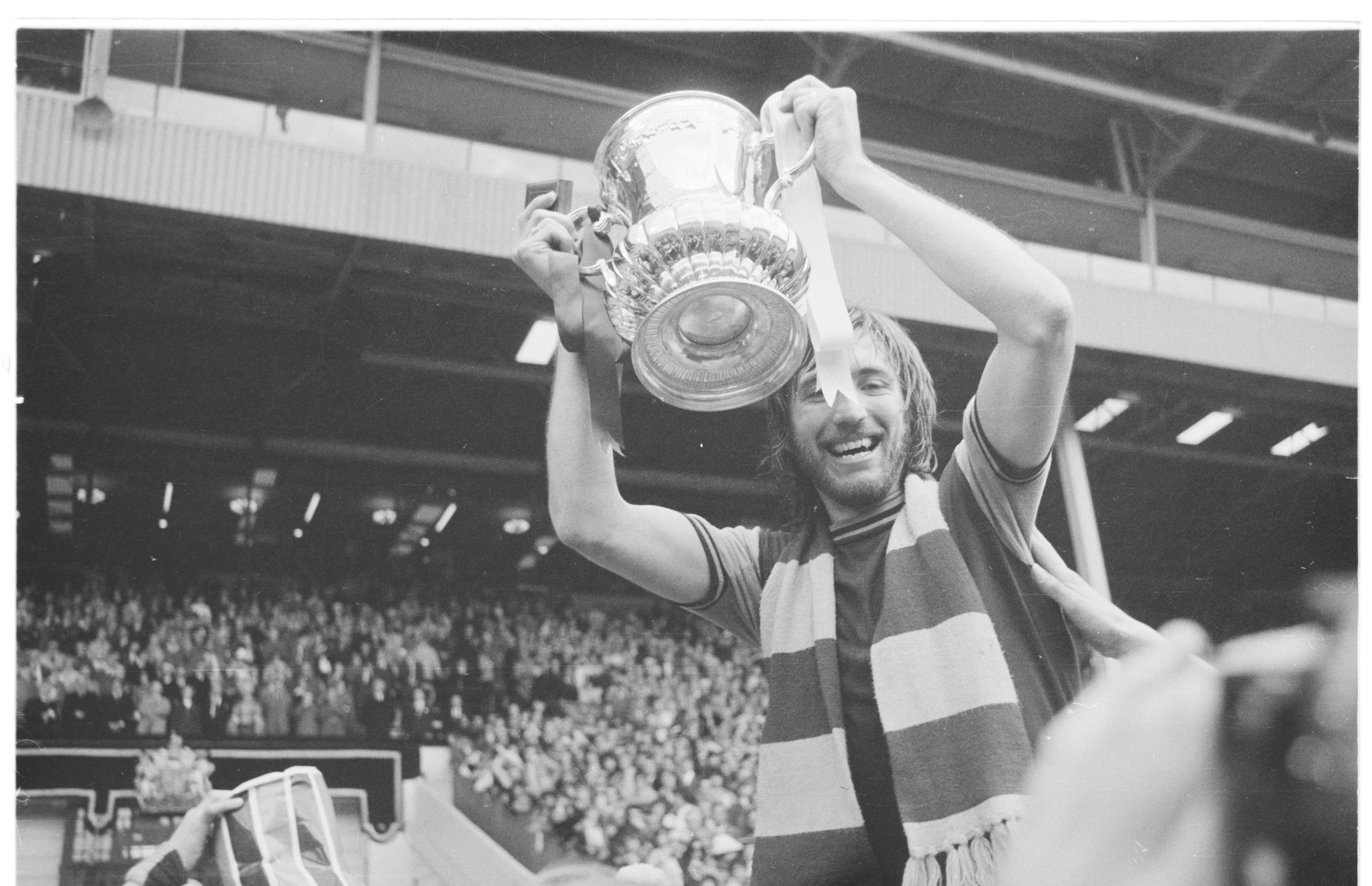 Footballer holding up the FA Cup trophy in a stadium.