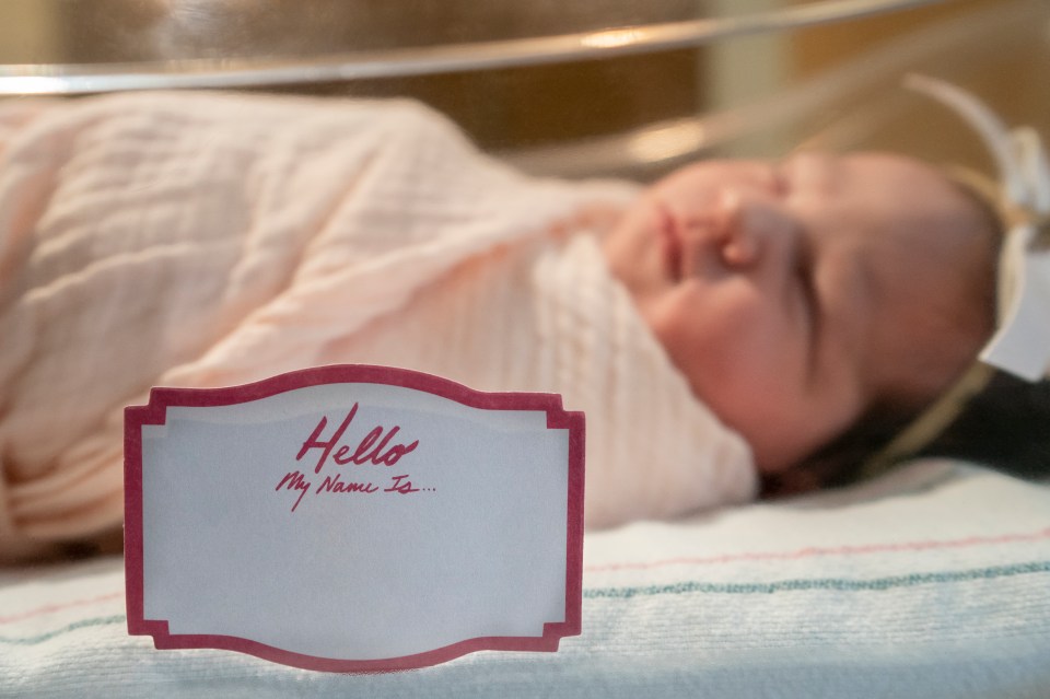 "Hello My Name Is..." name tag in front of a newborn baby in a hospital nursery.