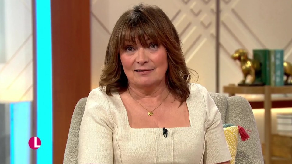 Lorraine Kelly, wearing a light-colored top and a heart-shaped necklace, looks at the camera.