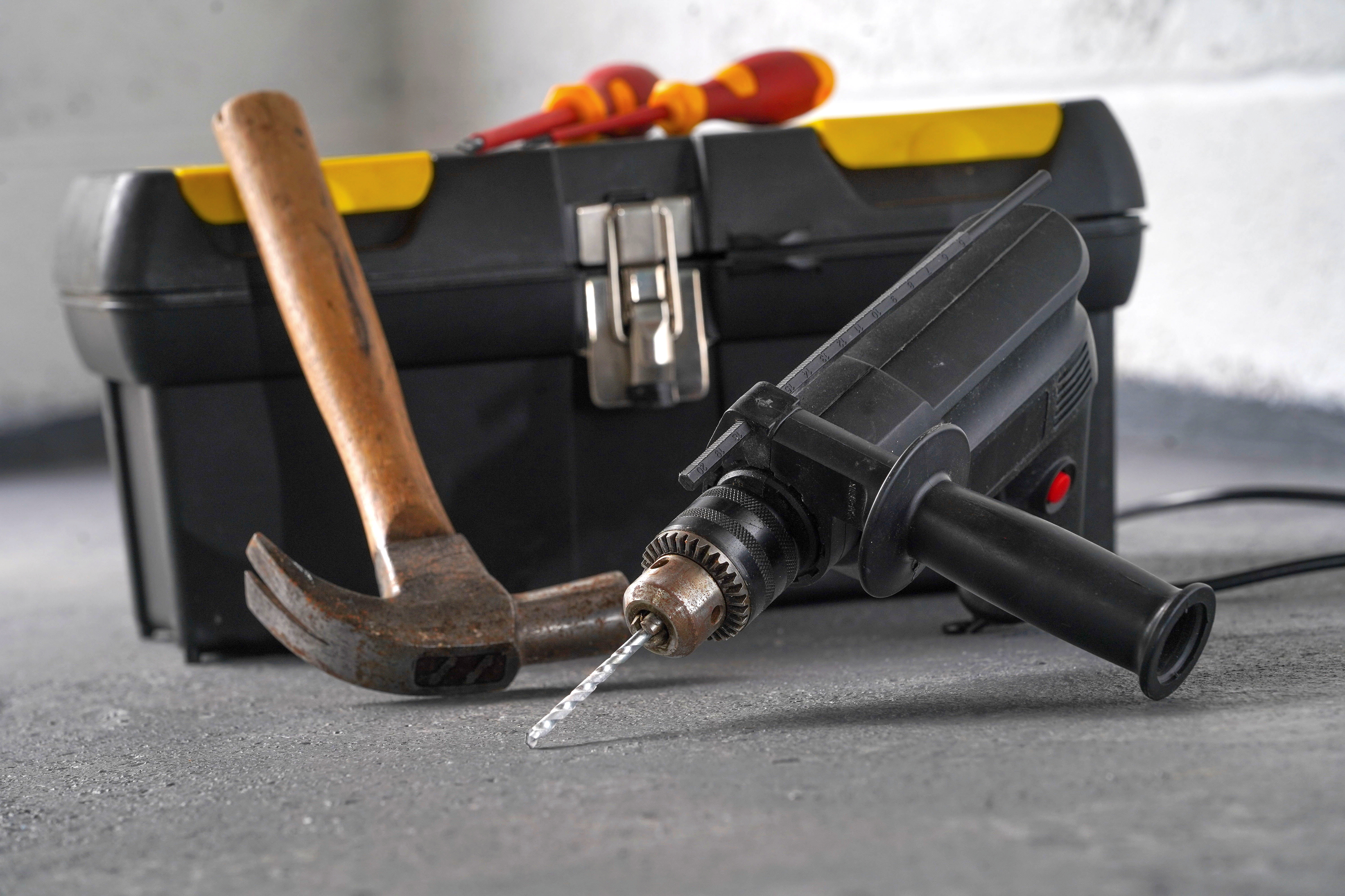Hammer, drill, and toolbox on a workbench.