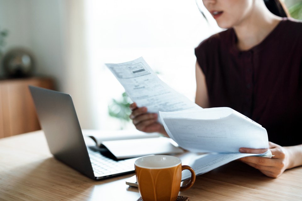 Woman reviewing financial documents with a laptop and coffee cup on the table.