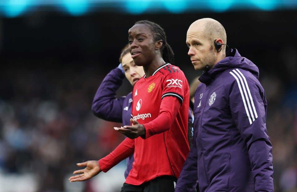 Manchester United player, wearing a red jersey, with a visible bump on her forehead, being attended to by team staff.