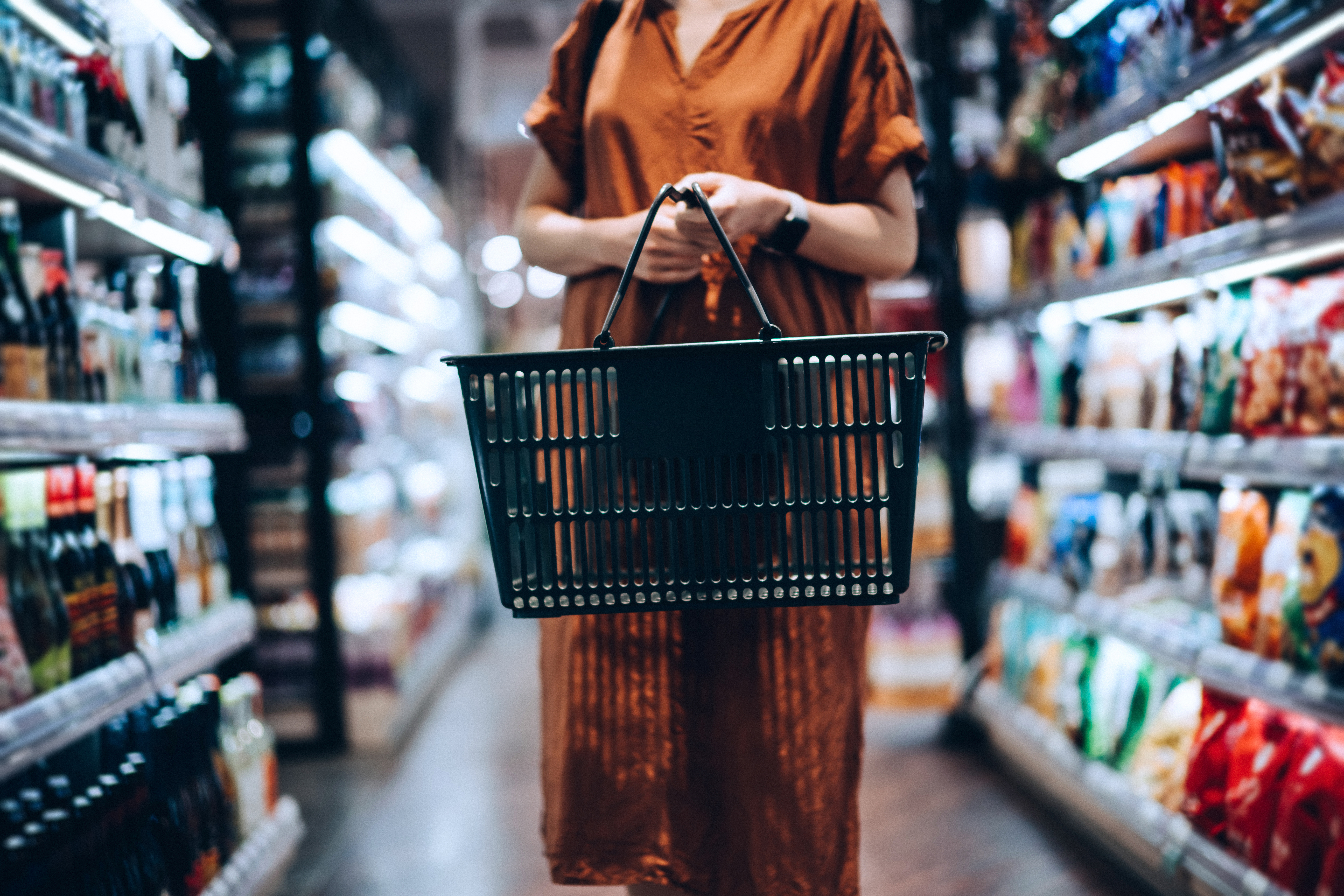 Woman carrying a shopping basket in a supermarket aisle.