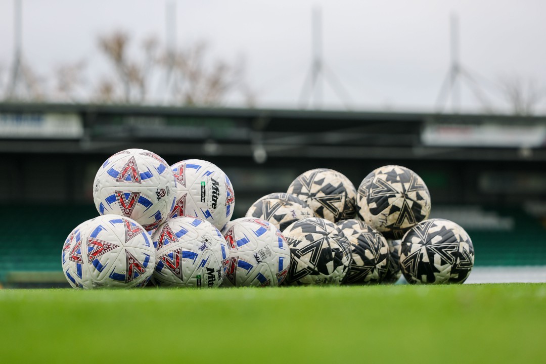 A pile of white, red and blue soccer balls, and a pile of black and white soccer balls on a green field.