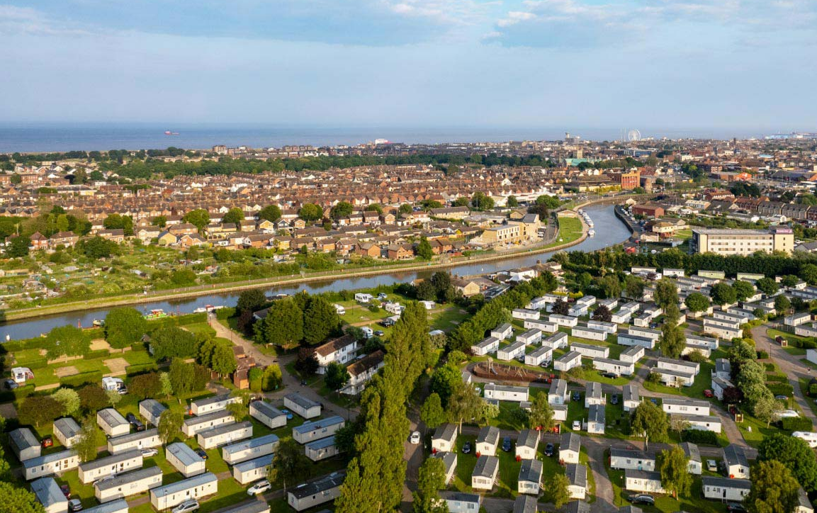 Aerial view of Vauxhall Holiday Park with mobile homes, a river, and a town leading to the sea.