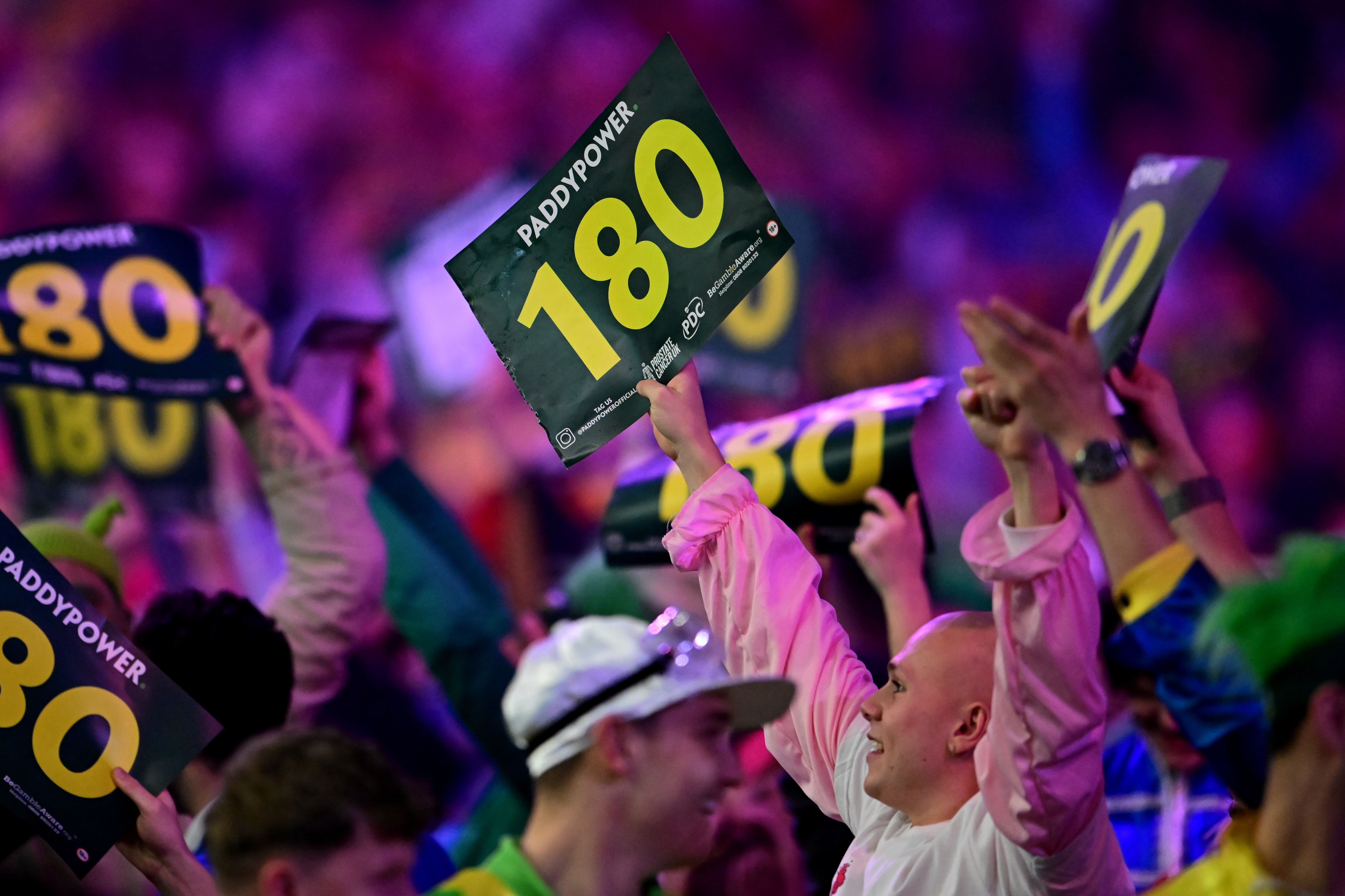 People holding "180" signs from Paddy Power at a darts event.