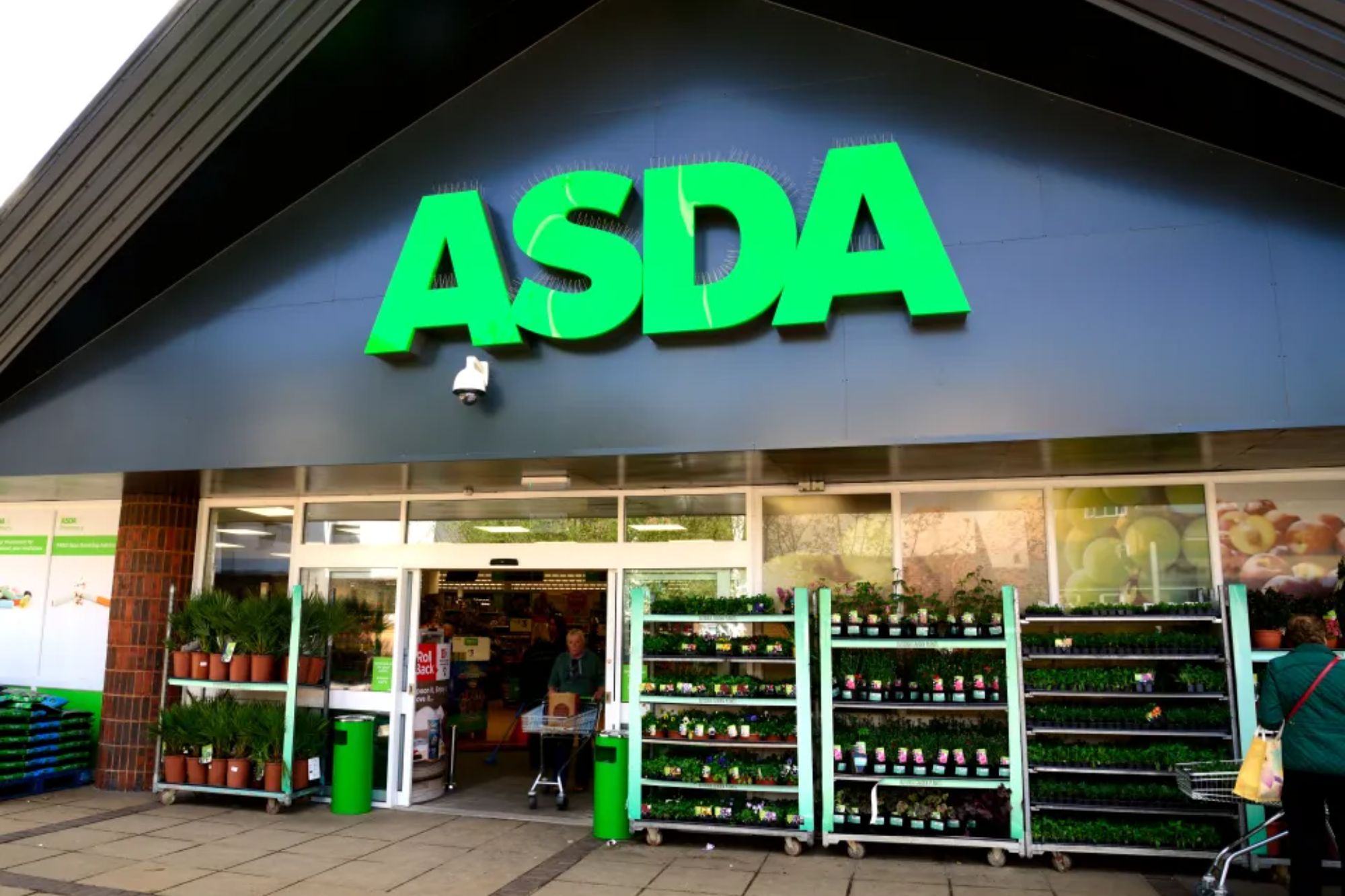 An image collage containing 1 images, Image 1 shows Exterior of an Asda supermarket with a bright green logo above the entrance and plants displayed outside