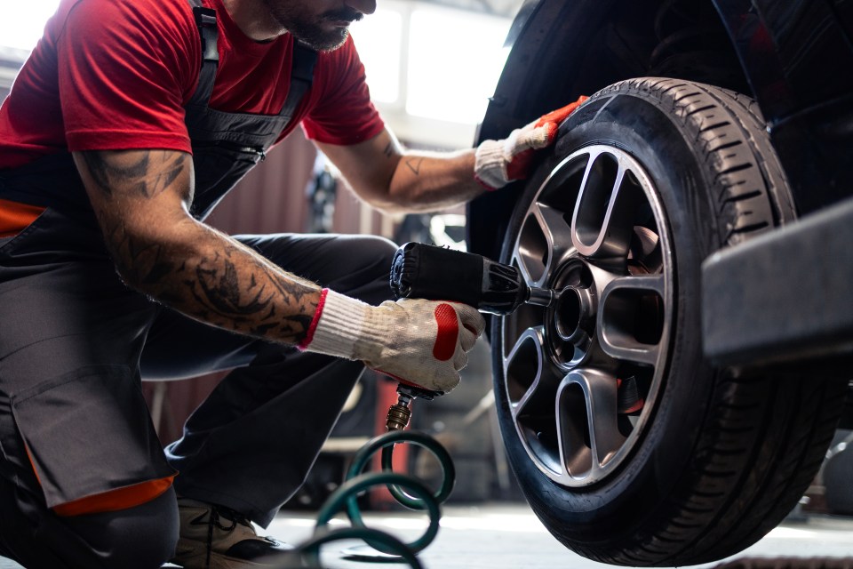 Mechanic using a pneumatic wrench to remove a car tire.