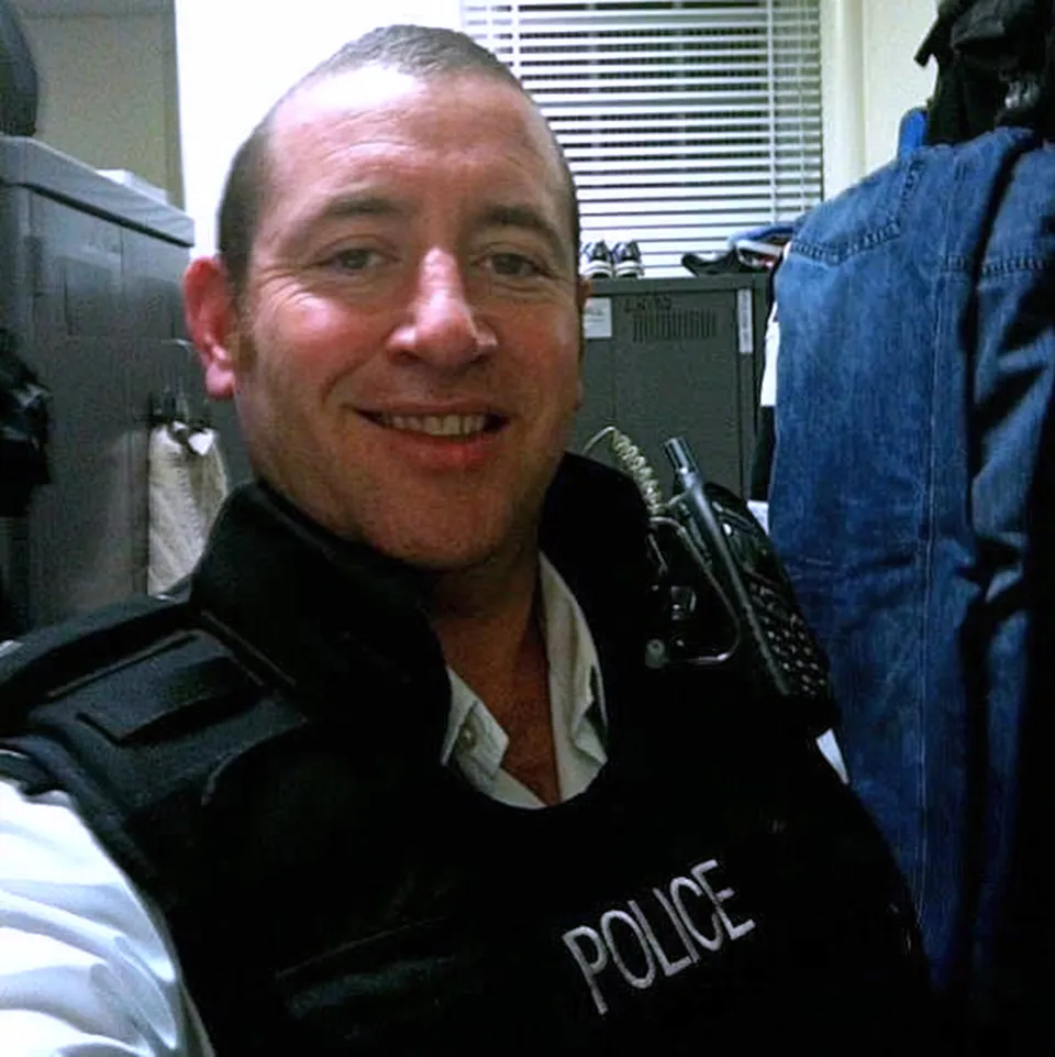 A man in a police vest smiling at the camera.