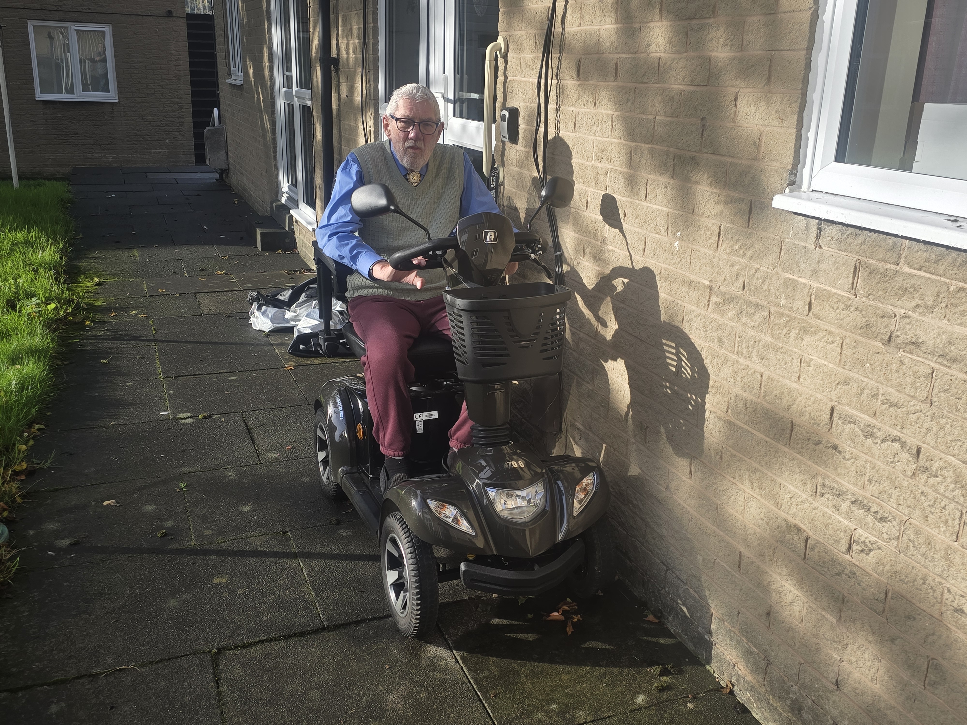 Ron Gibbs, 90, sits on his mobility scooter outside his housing association flat.
