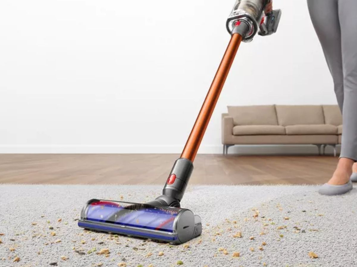 A person vacuuming a dirty carpet with a stick vacuum cleaner.
