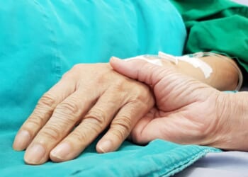 An oncologist holds the hand of a patient in a hospital.