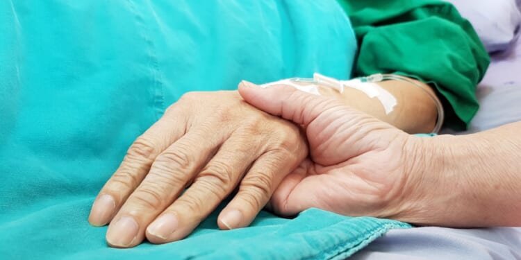 An oncologist holds the hand of a patient in a hospital.