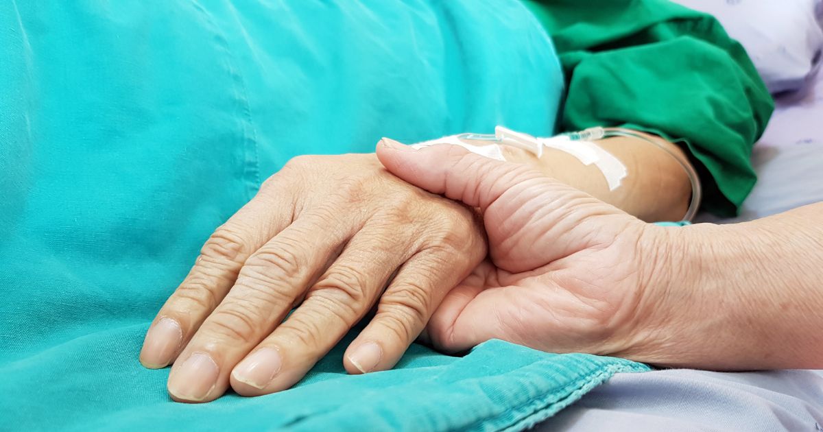 An oncologist holds the hand of a patient in a hospital.