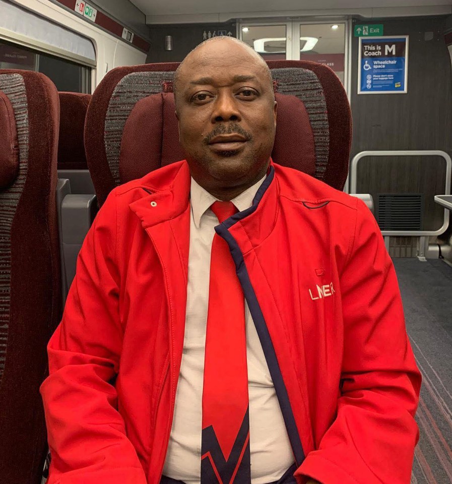 Amadu Bangura, a train staff member, wearing a red jacket and red tie, sitting on a train.