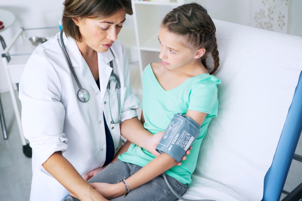 A female doctor taking a girl's blood pressure.