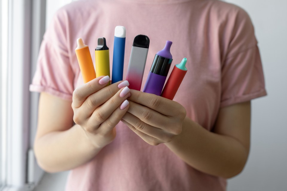 A woman holds a fan of six colorful electronic cigarettes.