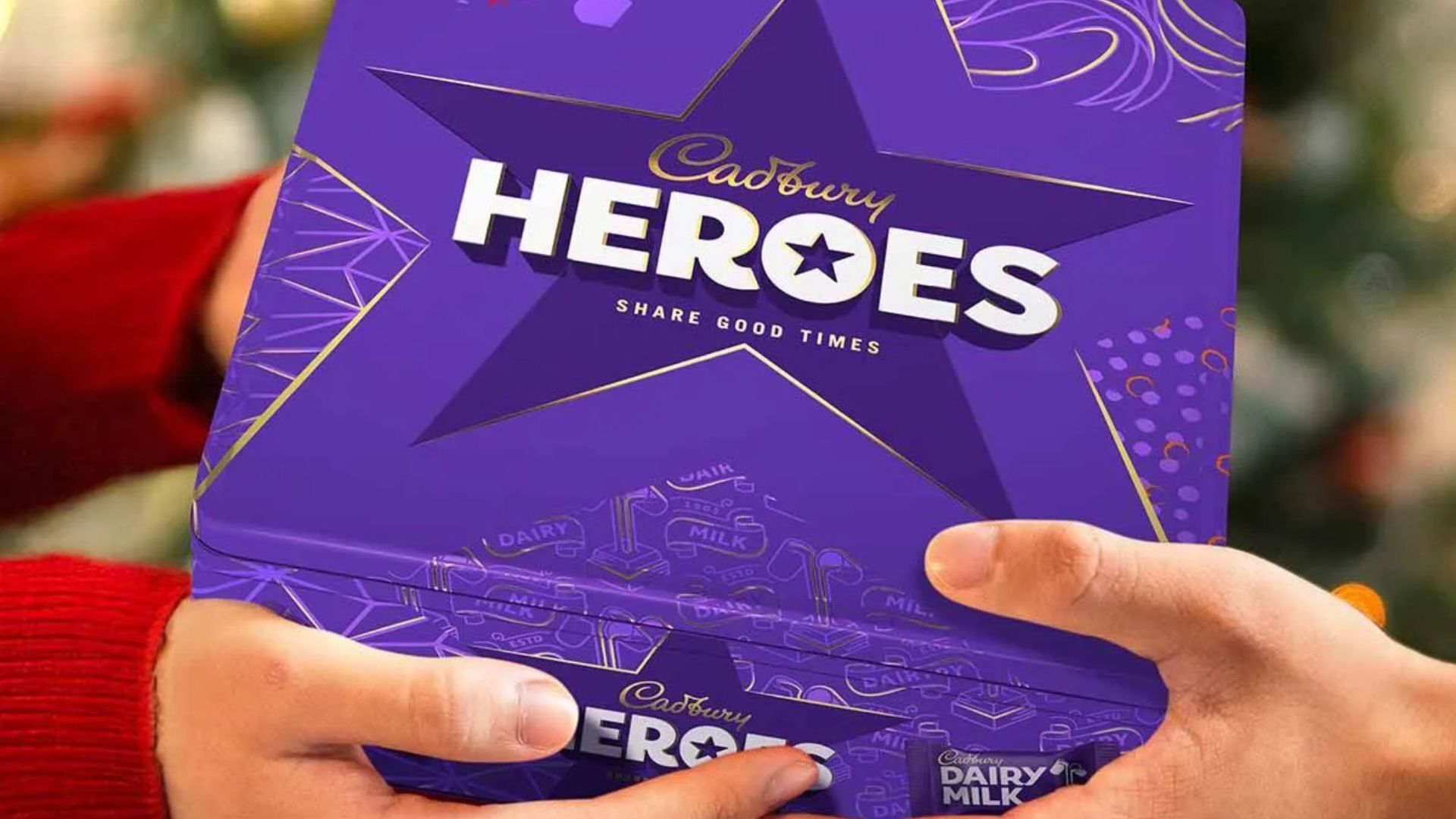 Hands holding a purple Cadbury Heroes chocolate box.