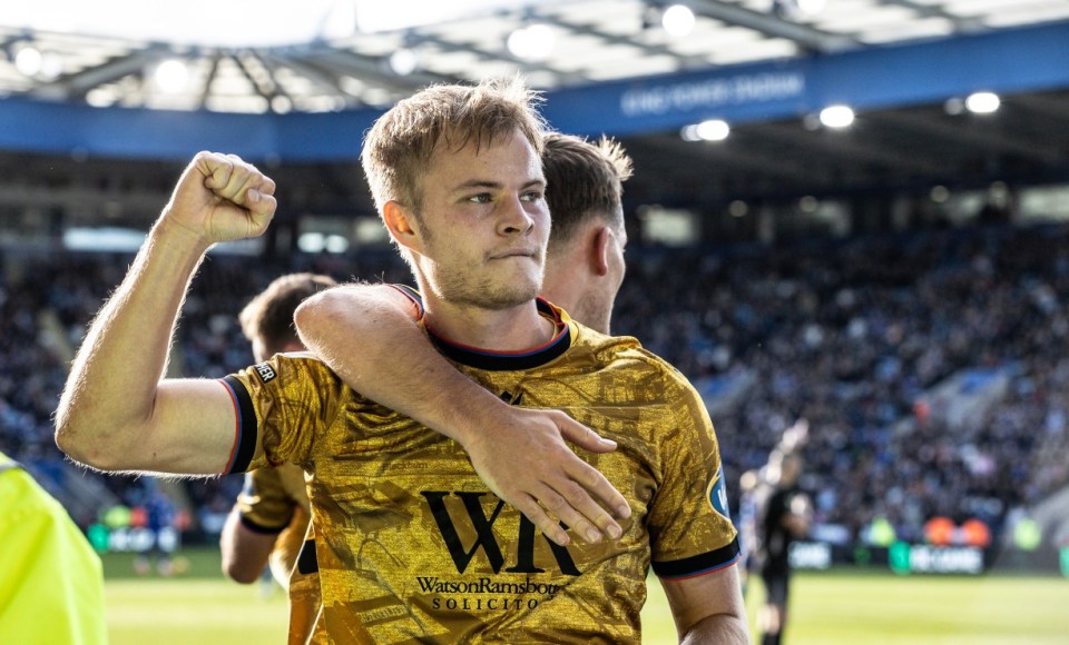 Two soccer players embracing on the field, with one player clenching his fist in celebration.