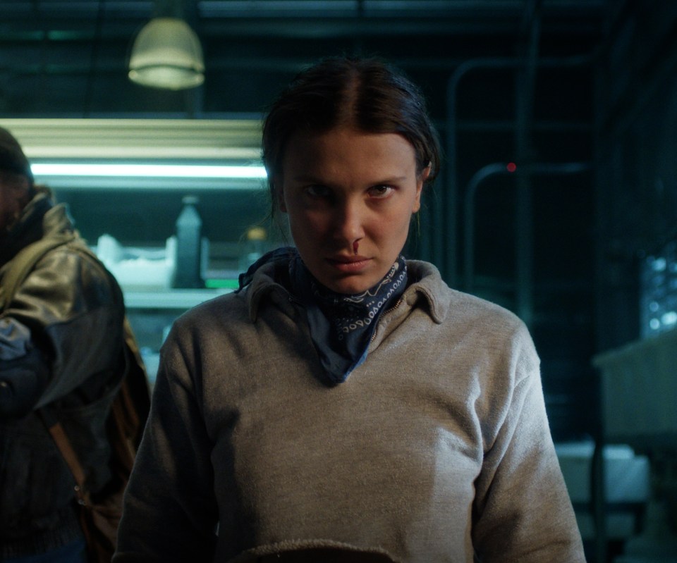 Eleven with a bloody nose in the foreground, and Jim Hopper holding a rifle in the background.