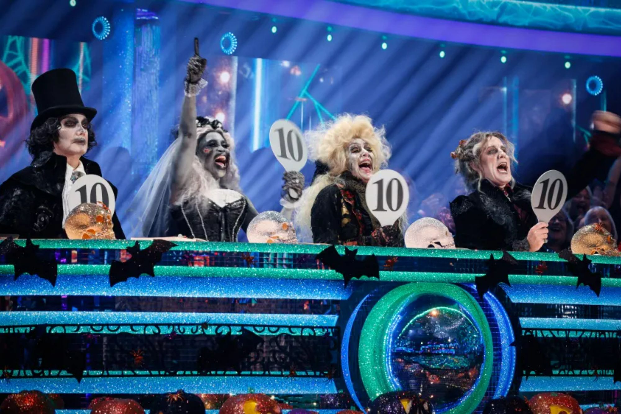 An image collage containing 1 images, Image 1 shows Craig Revel Horwood, Motsi Mabuse, Shirley Ballas, and Anton Du Beke dressed in Halloween costumes as judges on Strictly Come Dancing, all holding up signs with the number 10