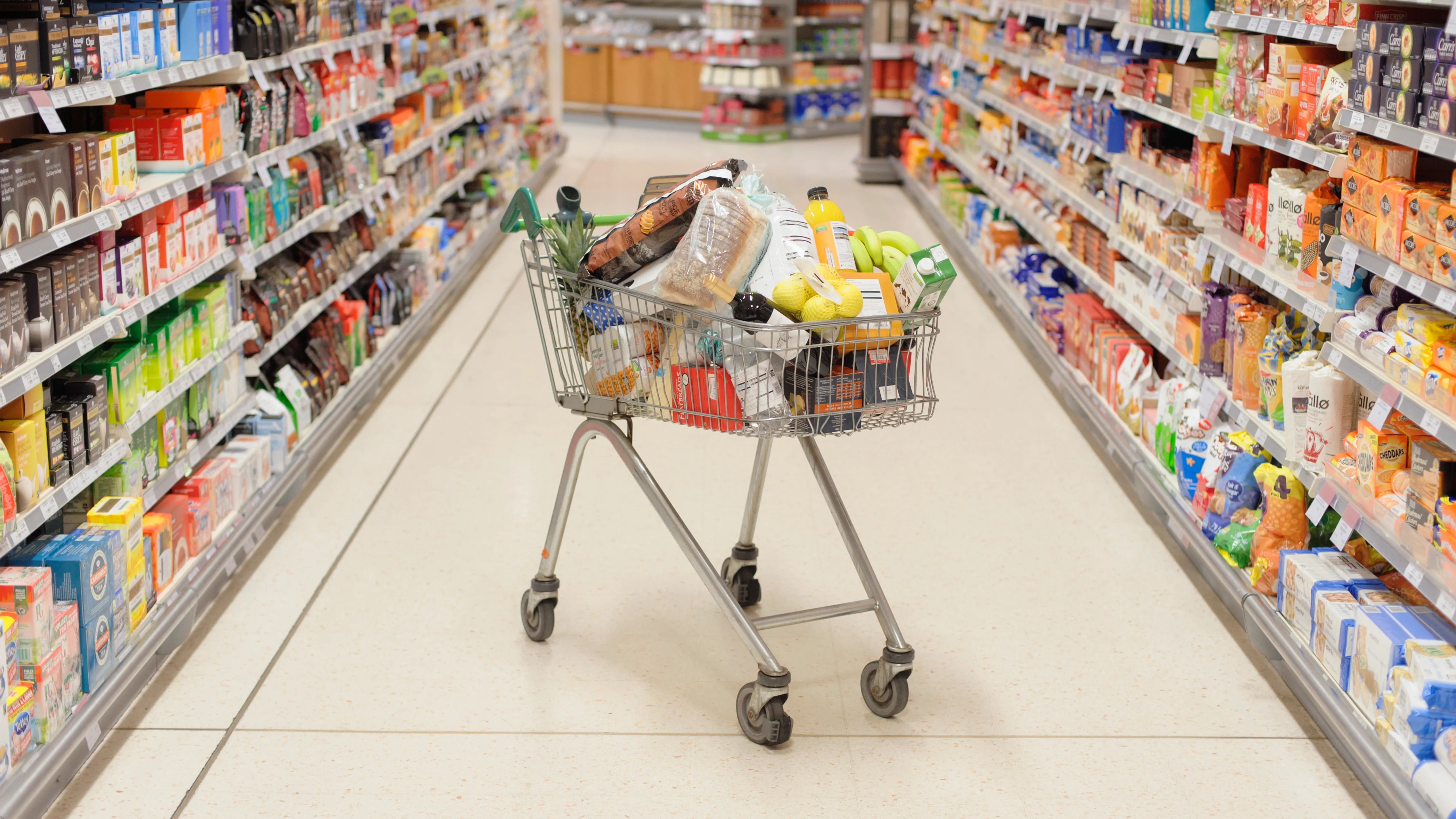 A full shopping cart in a supermarket aisle.