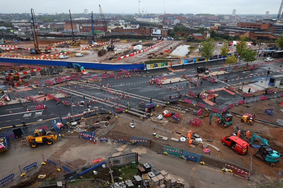 An aerial view of the HS2 high-speed railway construction site on Curzon Street in Birmingham, featuring cranes, construction vehicles, and workers amidst a network of roads and buildings under an overcast sky.