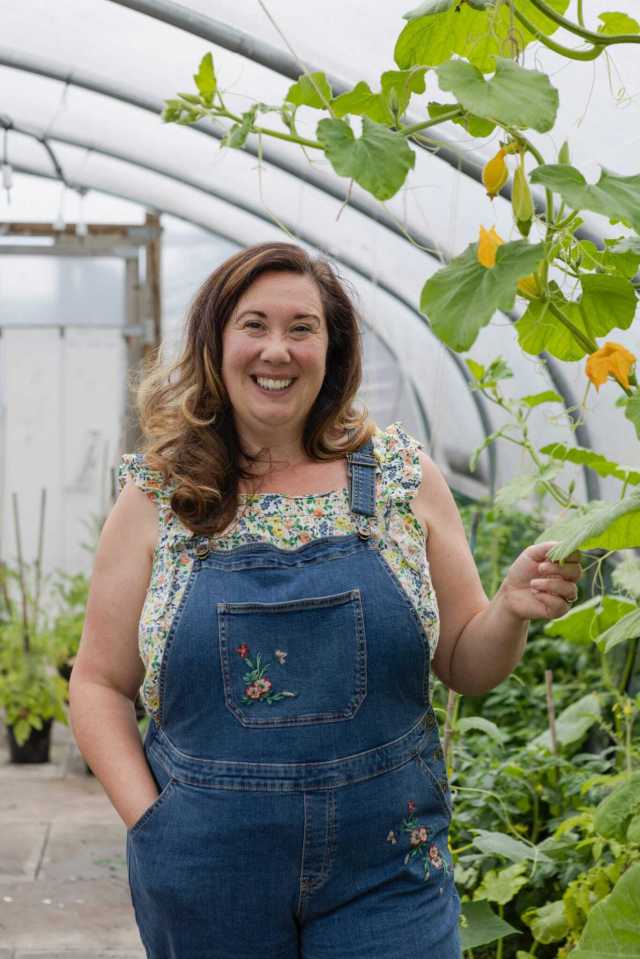Victoria Holden smiling in a greenhouse with blooming plants.