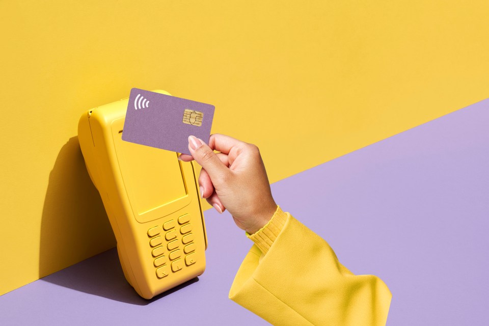 A person holding a purple credit card with a contactless chip above a yellow credit card POS terminal.