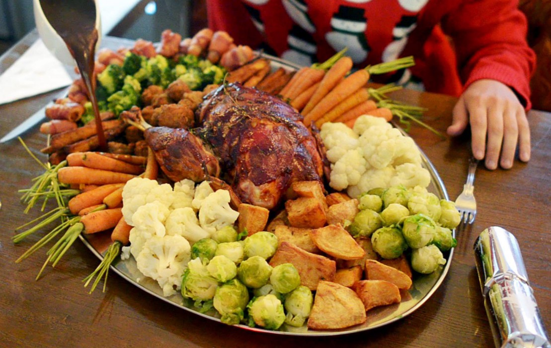 Gravy being poured over a roasted turkey and vegetables on a serving platter.