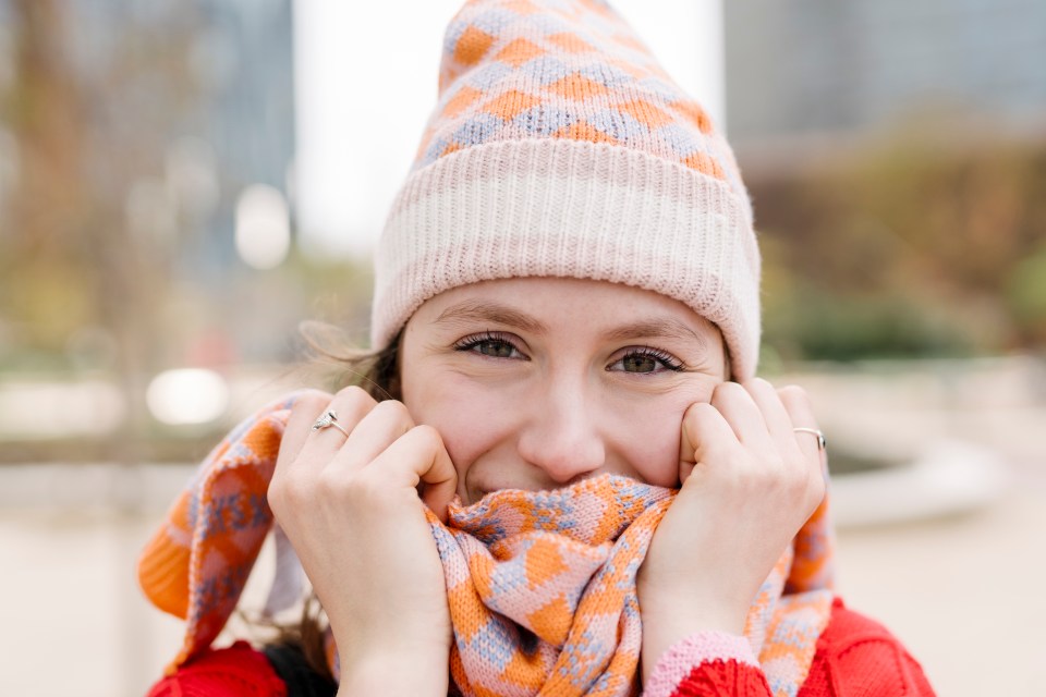 Young woman wearing a knit hat and scarf, smiling at the camera.