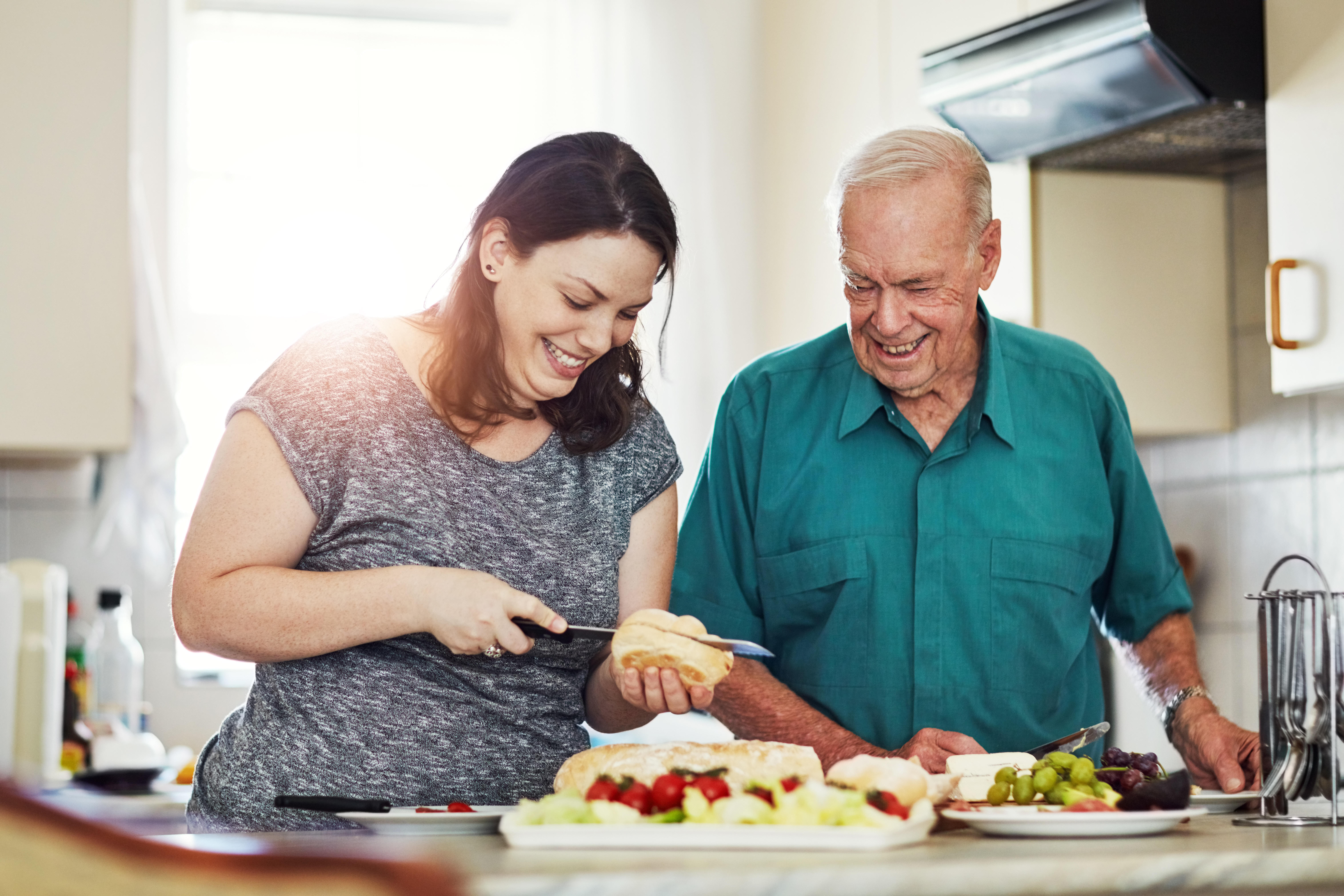 A younger woman and older man preparing food in a kitchen.