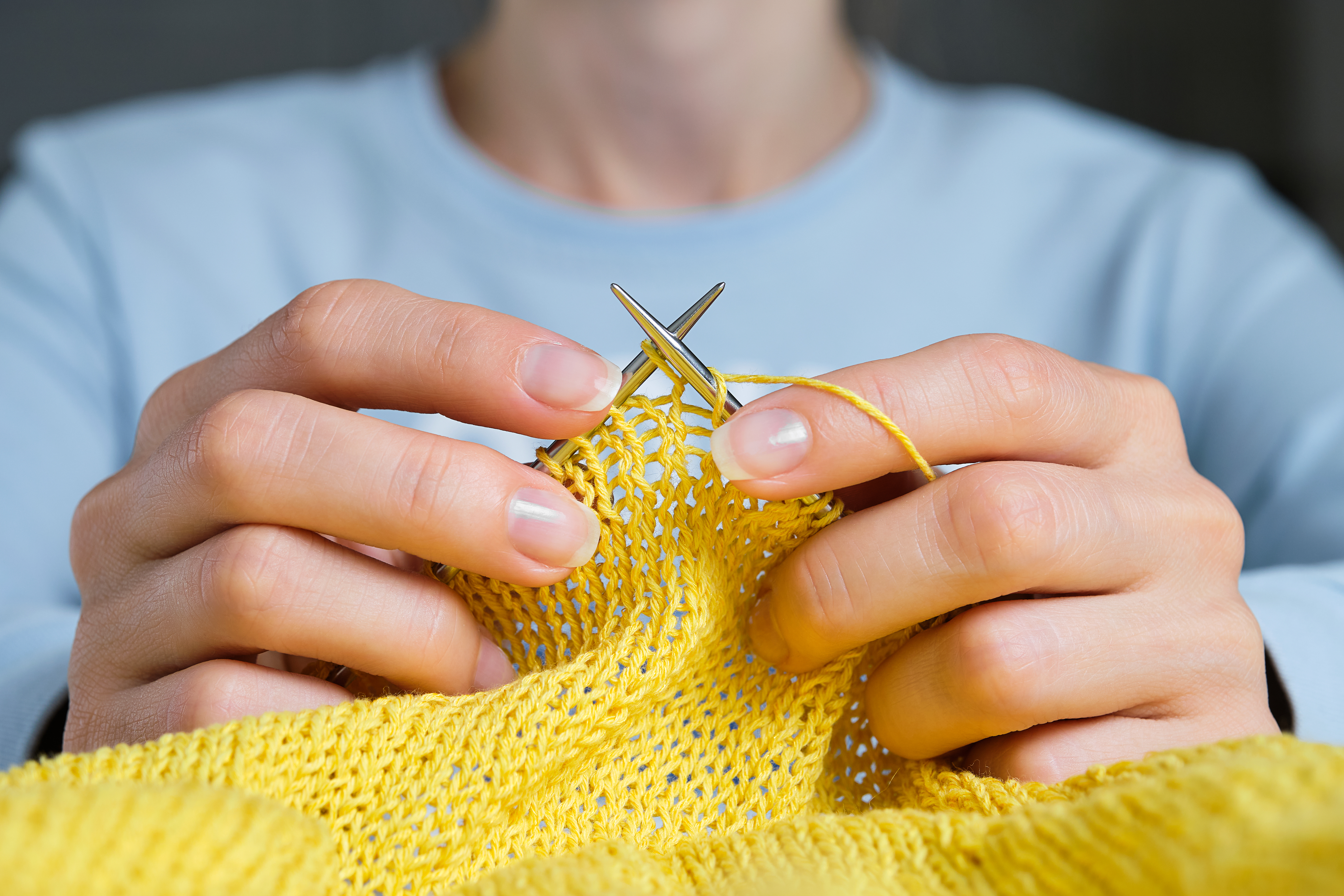 Hands knitting a yellow garment.