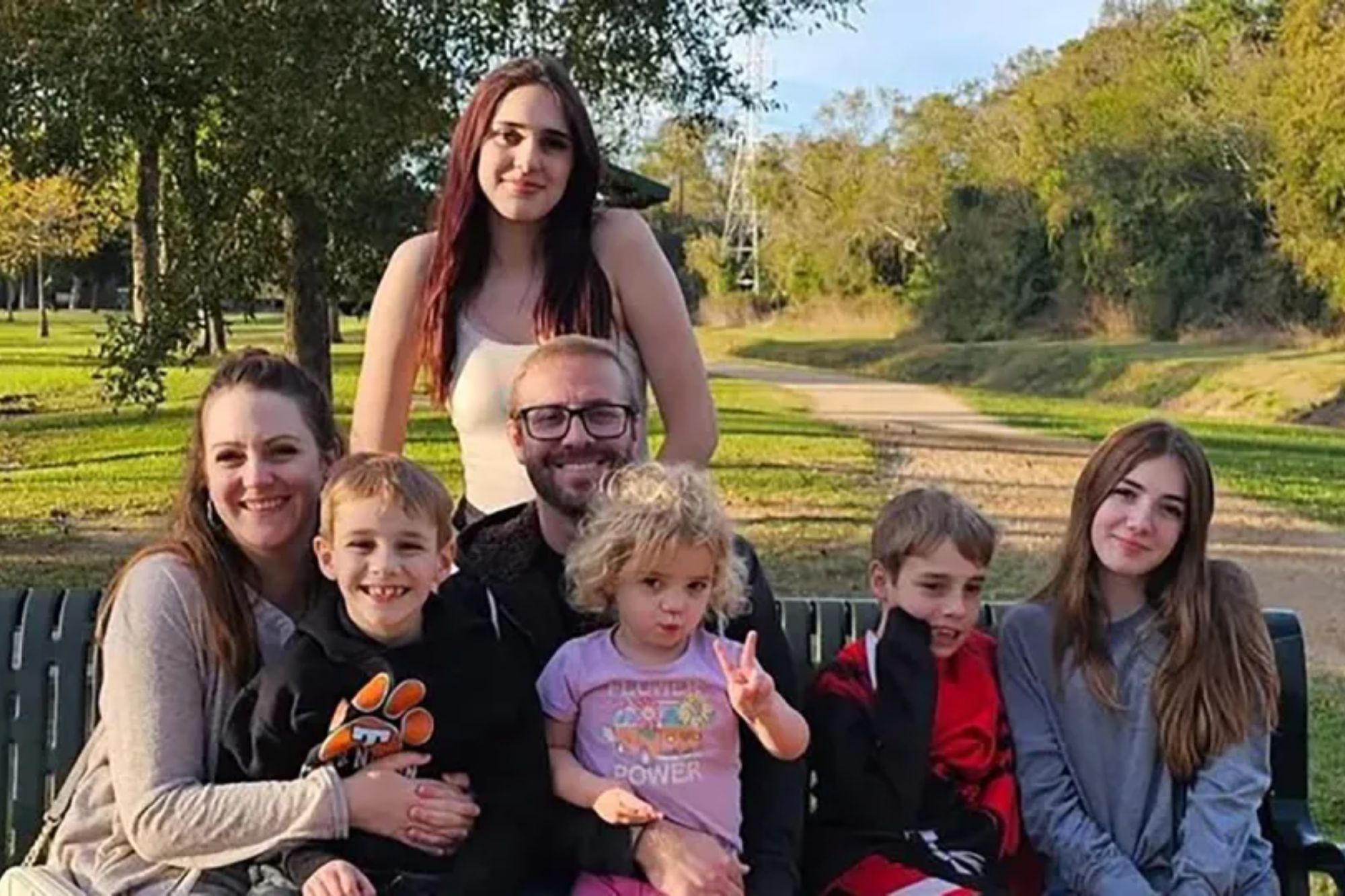 An image collage containing 1 images, Image 1 shows The Russell family, a couple with five children, sitting on a park bench