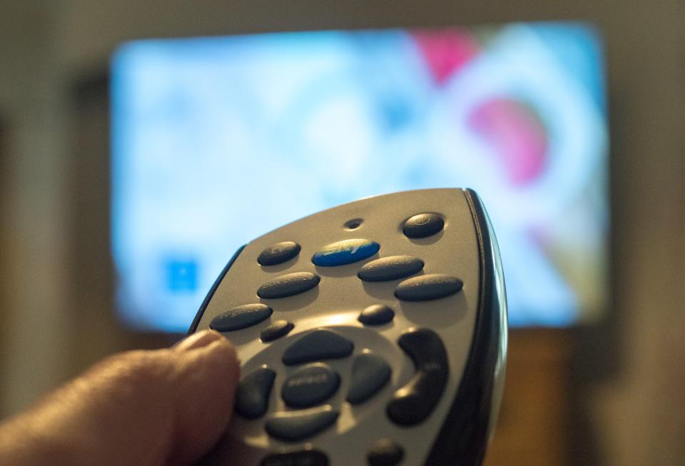 Close-up of a hand using a Sky TV remote.
