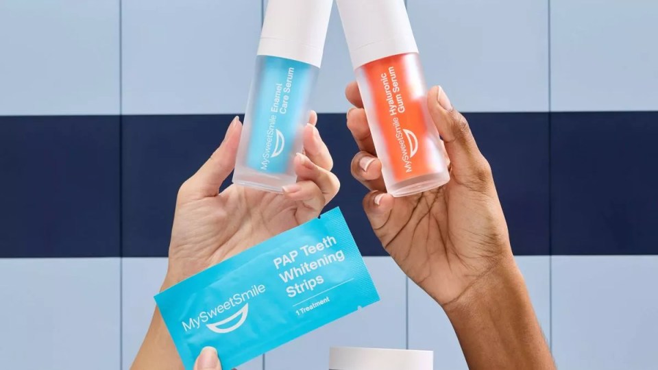 Two hands holding MySweetSmile Enamel Care Serum, MySweetSmile Hyaluronic Gum Serum, and MySweetSmile PAP Teeth Whitening Strips.