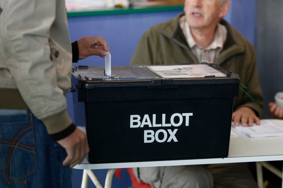 A voter places their ballot into a black ballot box.